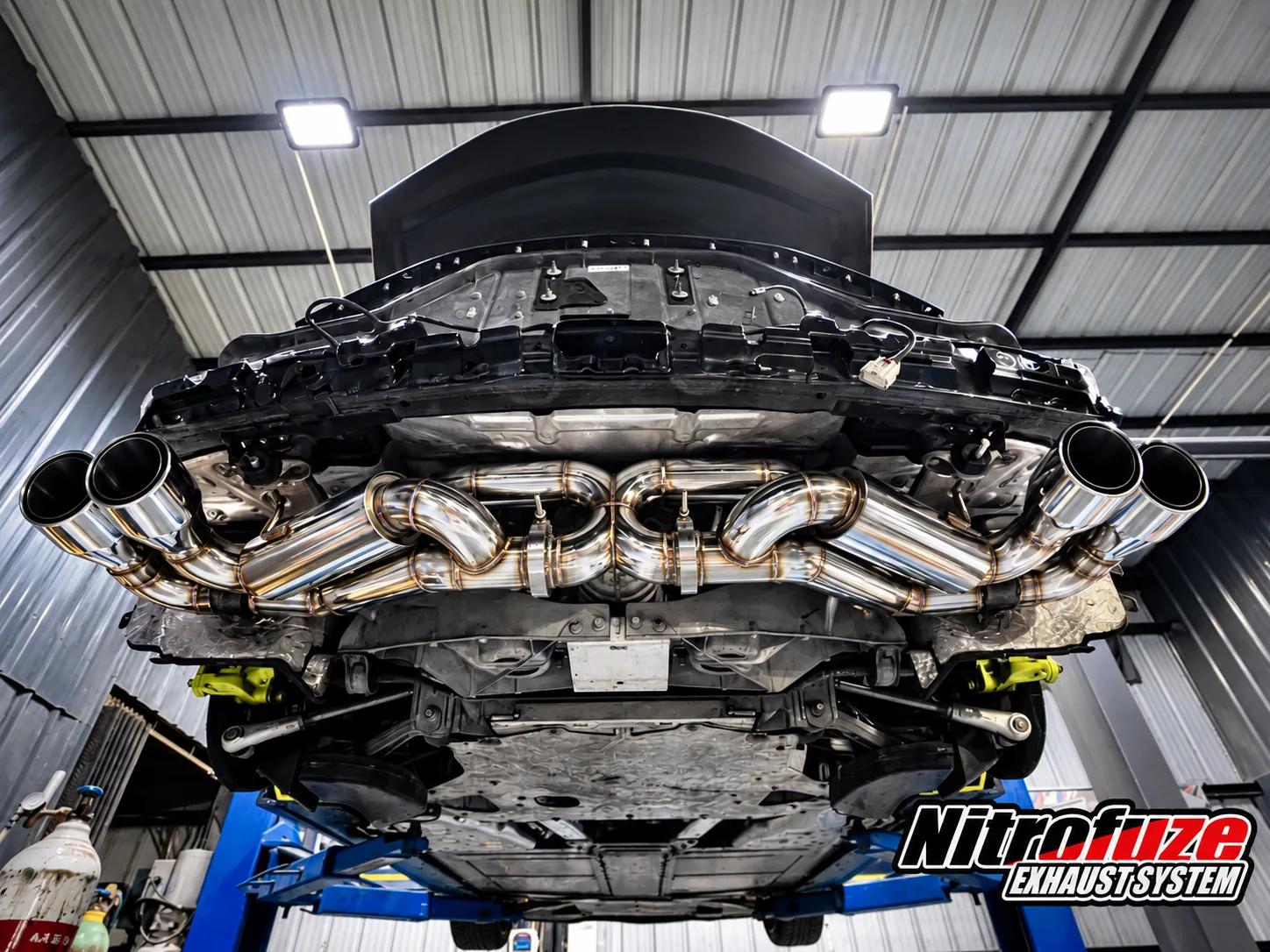 Quad stainless exhaust tips and a G-pipe catback system under a Corvette C6 on the lift