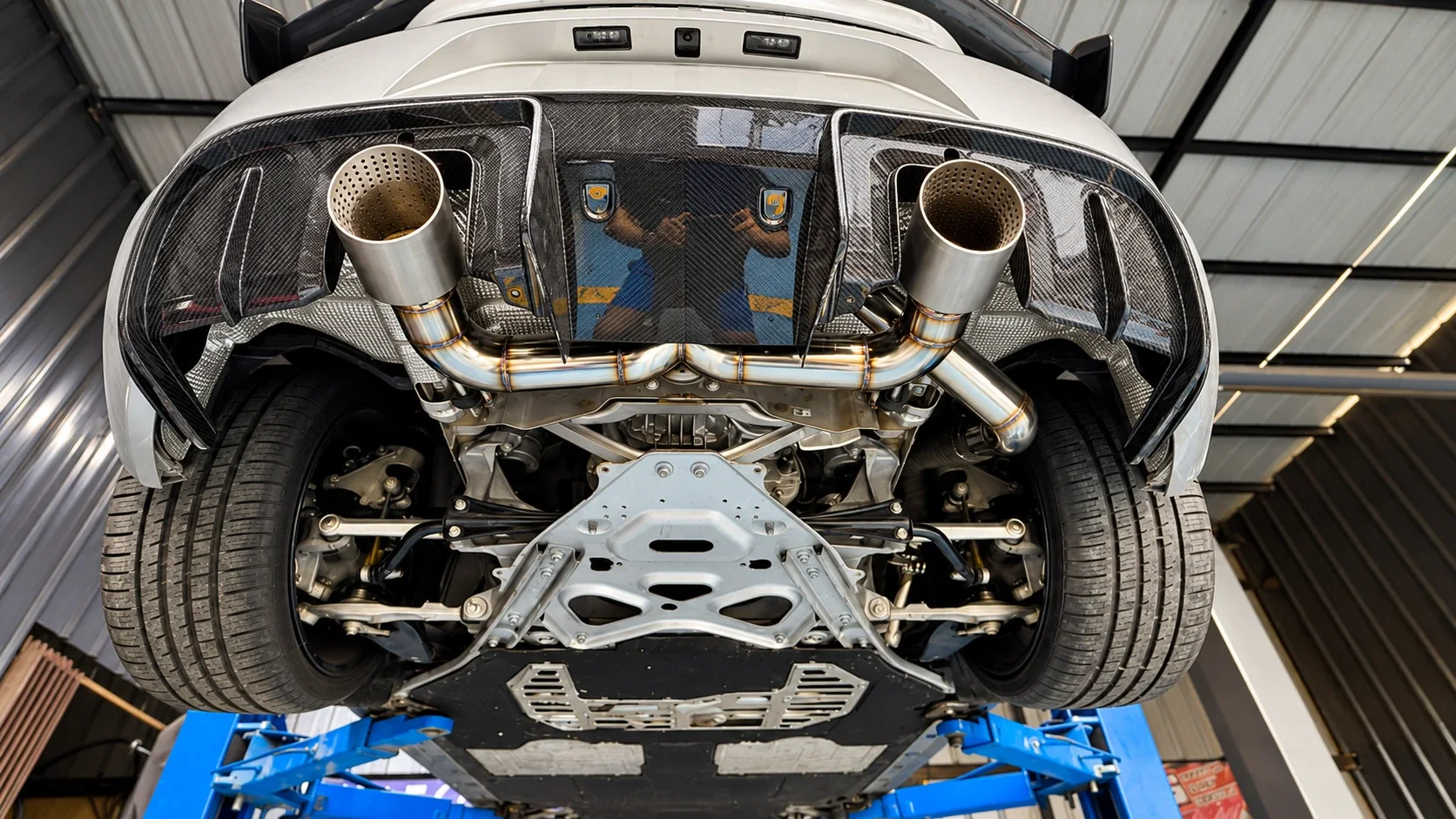 Underside of a Porsche GT4 on the lift showing the stainless full straight-pipe exhaust with custom downpipe