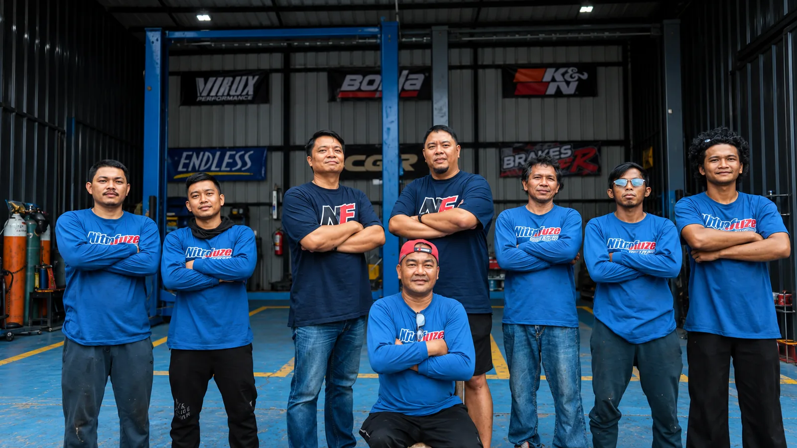 The Nitrofuze Garage crew in blue Nitrofuze shirts, standing in the fabrication bay with the owners