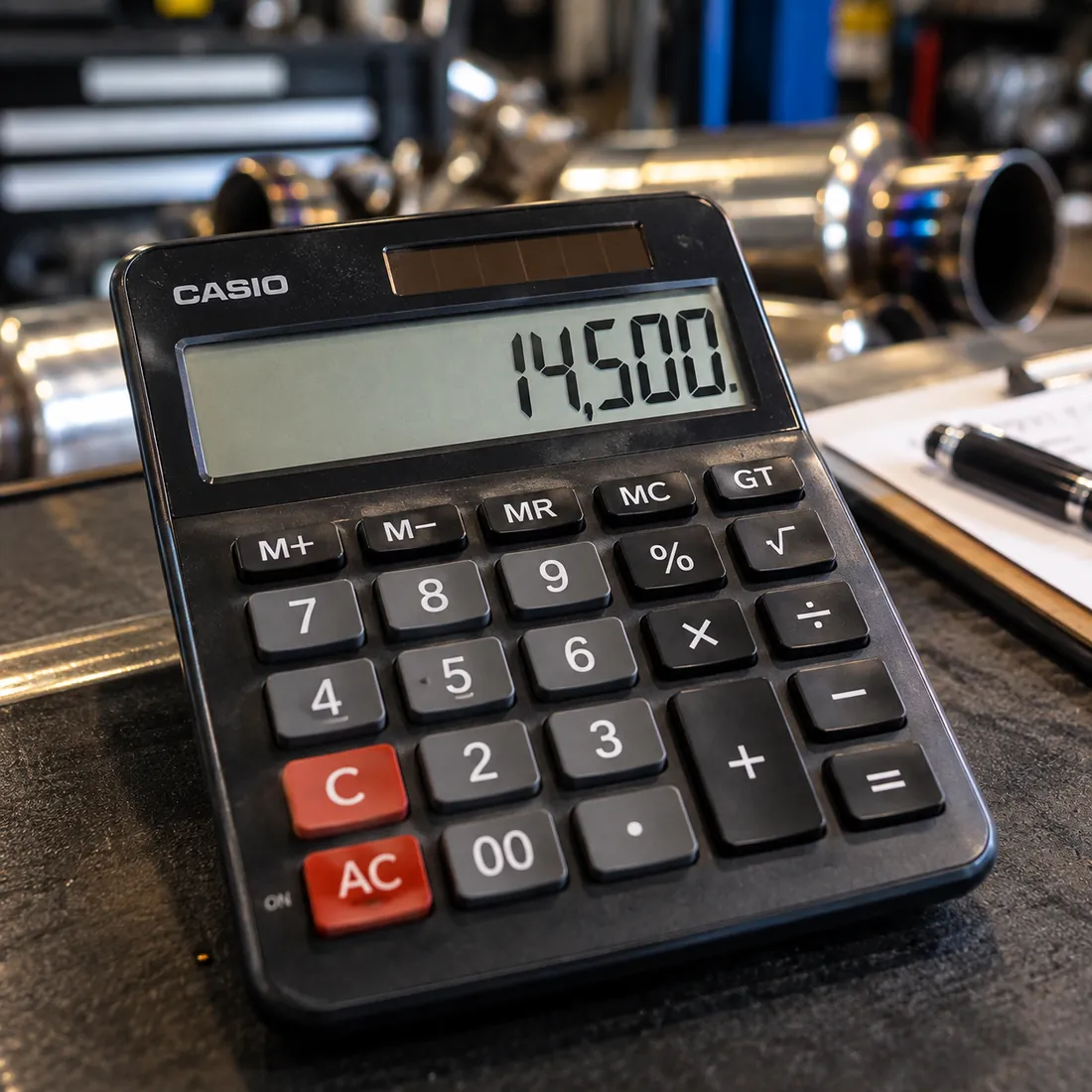 A calculator on the workbench beside exhaust parts